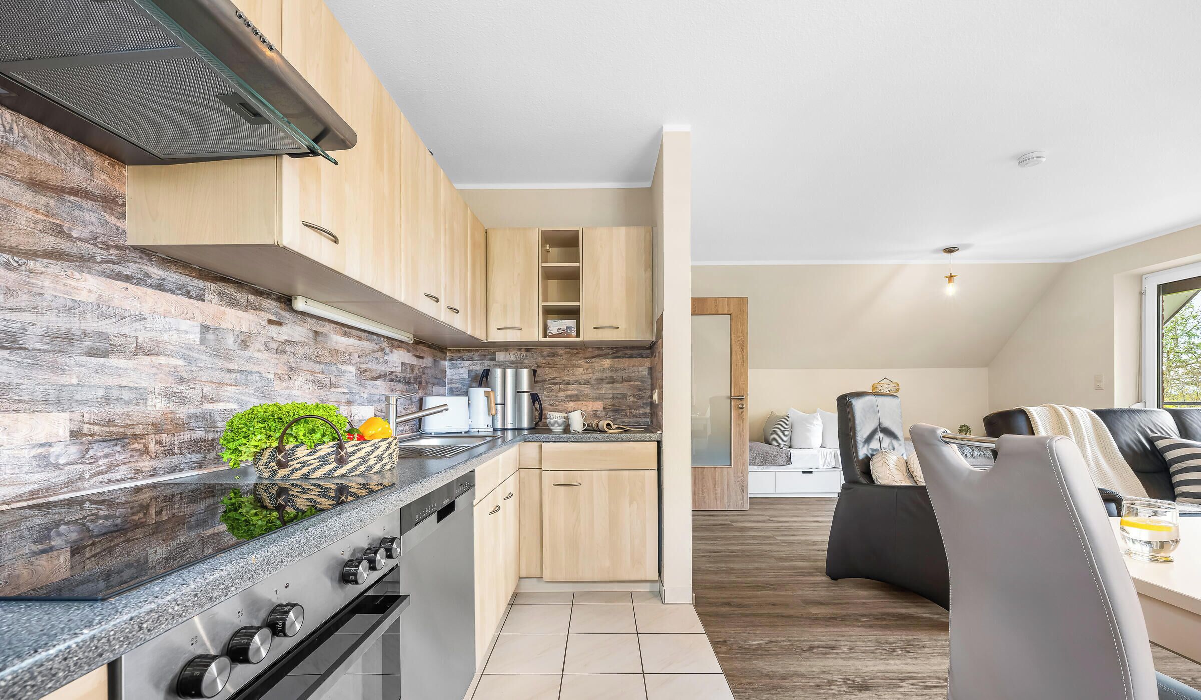 Eine moderne Küche mit Holzschränken, einem eingebauten Backofen und einer Arbeitsplatte mit Wasserkocher und Kaffeemaschine.