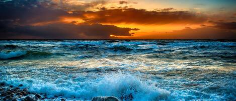 Une plage où les vagues s’écrasent contre les rochers, avec un coucher de soleil en arrière-plan.