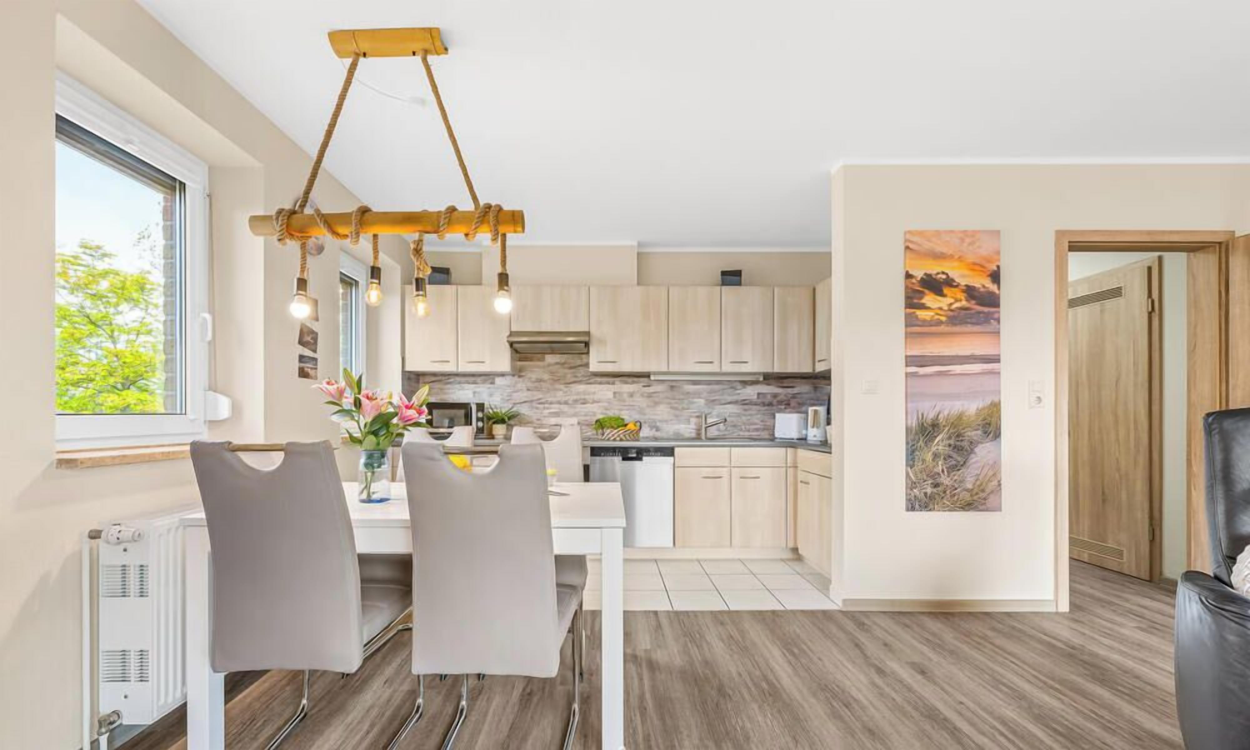 Una cucina moderna con zona pranzo, caratterizzata da un'isola centrale, illuminazione a sospensione e vista sull'esterno.