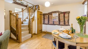 Un escalier en bois mène à une salle à manger où une table est dressée pour le petit-déjeuner, avec un mur en pierre et un radiateur.