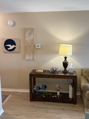 A living room with a wooden coffee table, a lamp, decorative items, and a wall-mounted thermostat. - 1BR/1BA condo in Pensacola near Perdido Key, sleeps 4. (Perdido Key)