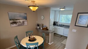 A dining area with a round table and chairs, a kitchen in the background, and a clock on the wall. - D 32 Sundown Condominiums (Perdido Key)