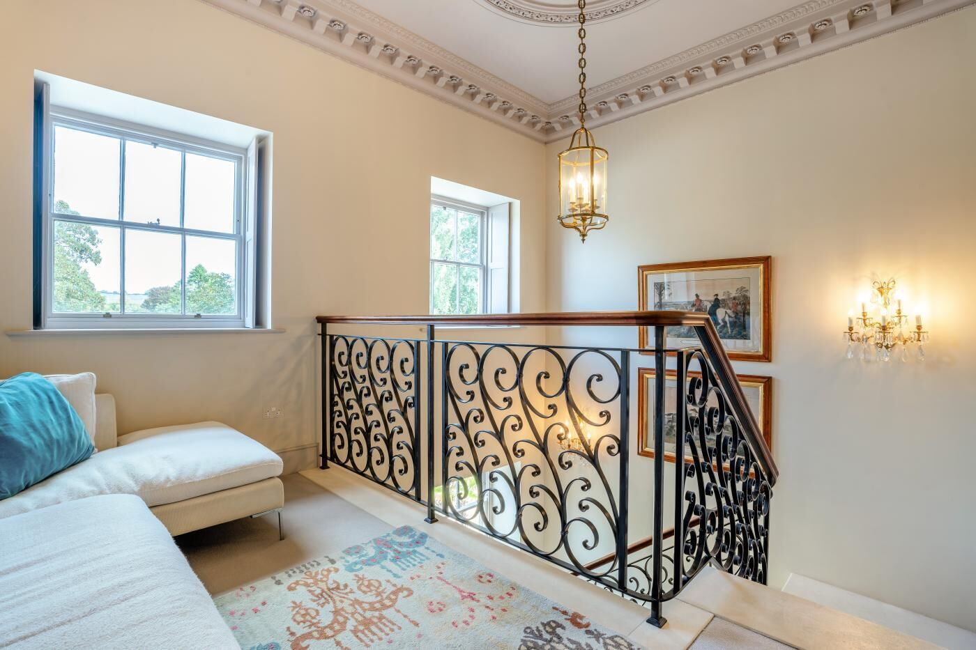 A room with a sofa, a patterned rug, a staircase with ornate railings, and a chandelier.