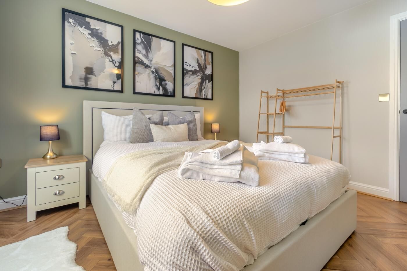 Une chambre à coucher avec un lit, des tables de chevet, une lampe, une échelle et des œuvres d’art abstraites accrochées au mur.