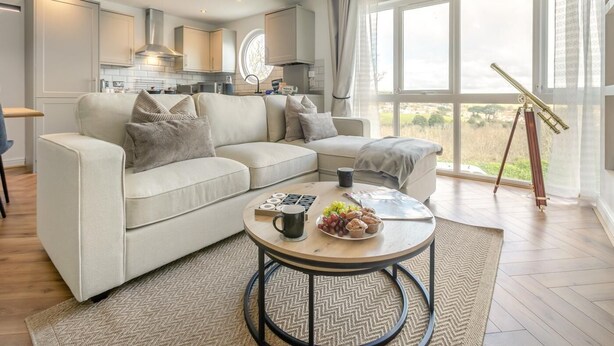 Ein modernes Wohnzimmer mit einer Eckcouch, einem Couchtisch mit Snacks, einem Teleskop und einem großen Fenster mit Ausblick.