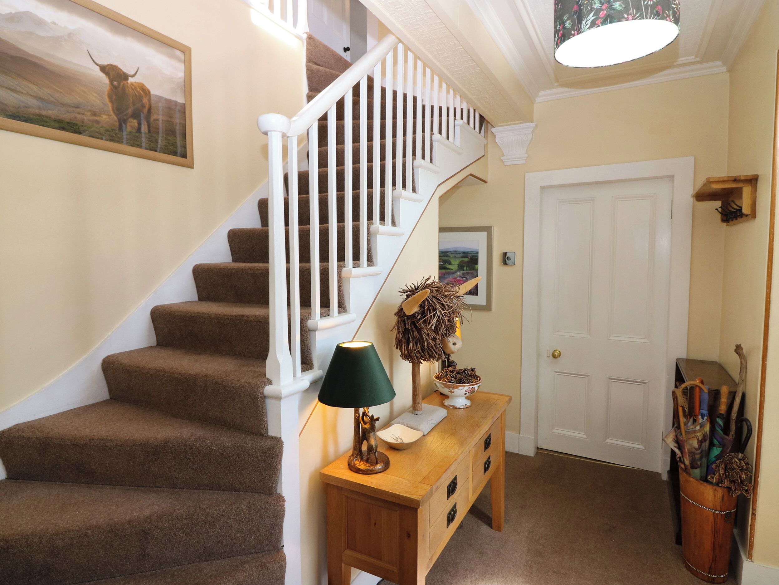 A staircase with brown carpeted steps, a wooden console table with a lamp, and a door with a picture frame.