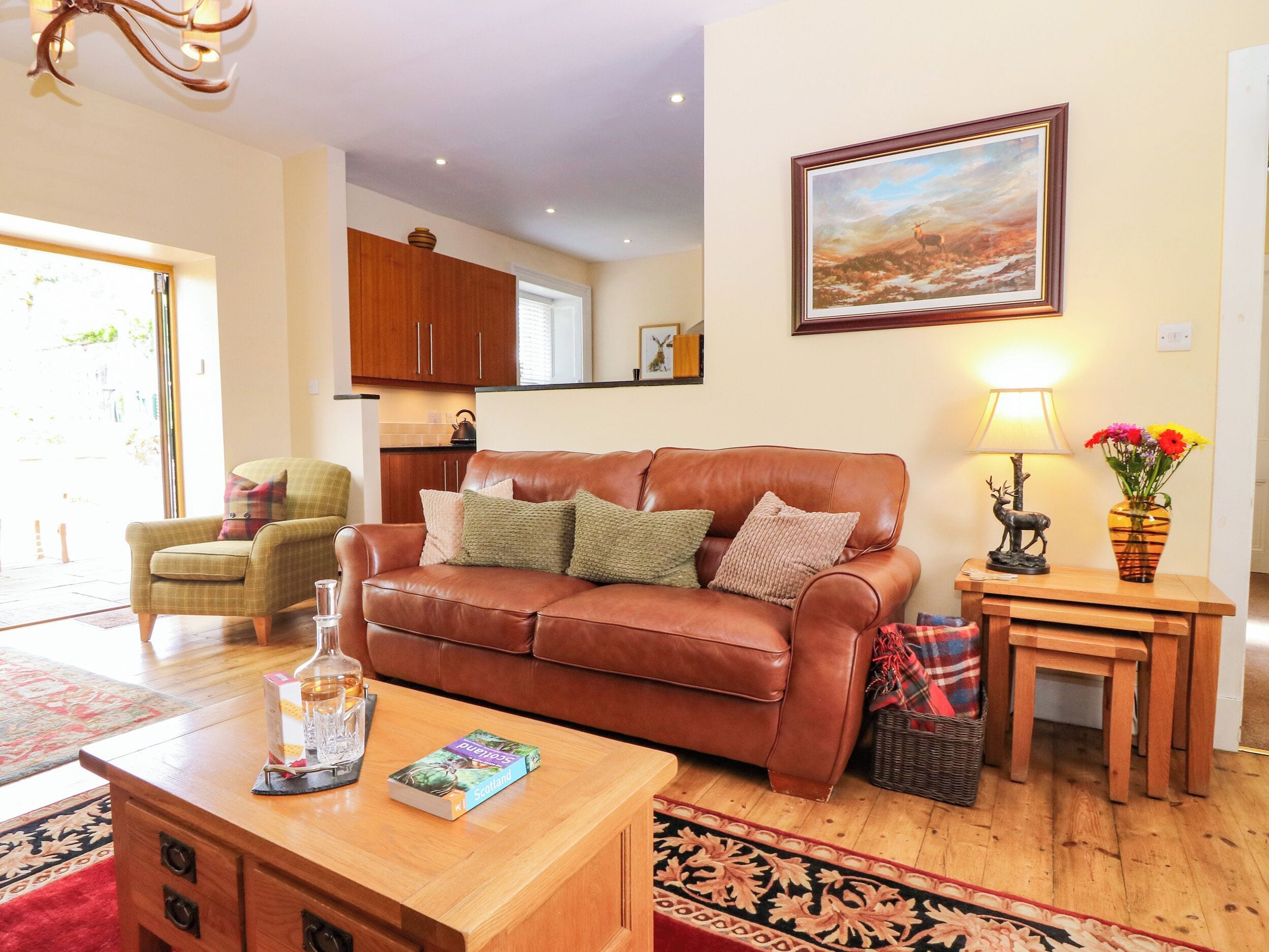 A living room with a brown leather sofa, a wooden coffee table, a lamp, and a vase with flowers.