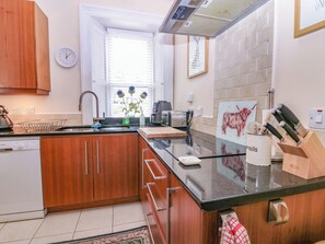 A modern kitchen with wooden cabinets, a black countertop, a sink, a coffee maker, and a knife block. - St Kilda (Ballater)