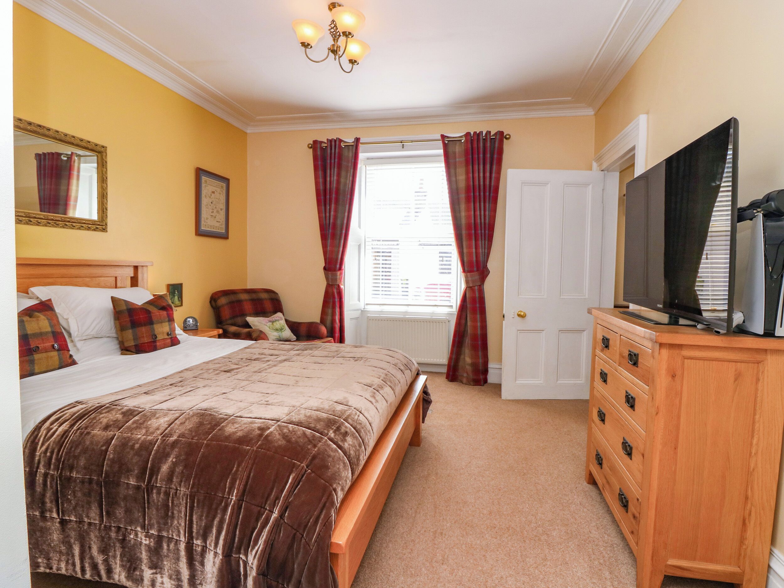 A bedroom with a bed, a chair, a dresser, a television, and a window with curtains.