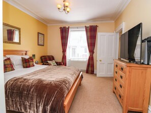 A bedroom with a bed, a chair, a dresser, a television, and a window with curtains. - St Kilda (Ballater)