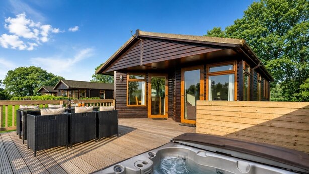 A wooden deck with a hot tub, outdoor furniture, and a building with large windows. - 2 Bed in Athelington (oc-a35072) (Athelington)