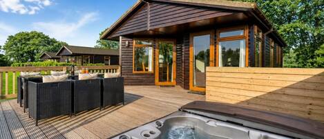 Une terrasse en bois avec un jacuzzi, du mobilier d’extérieur et un bâtiment doté de grandes fenêtres.