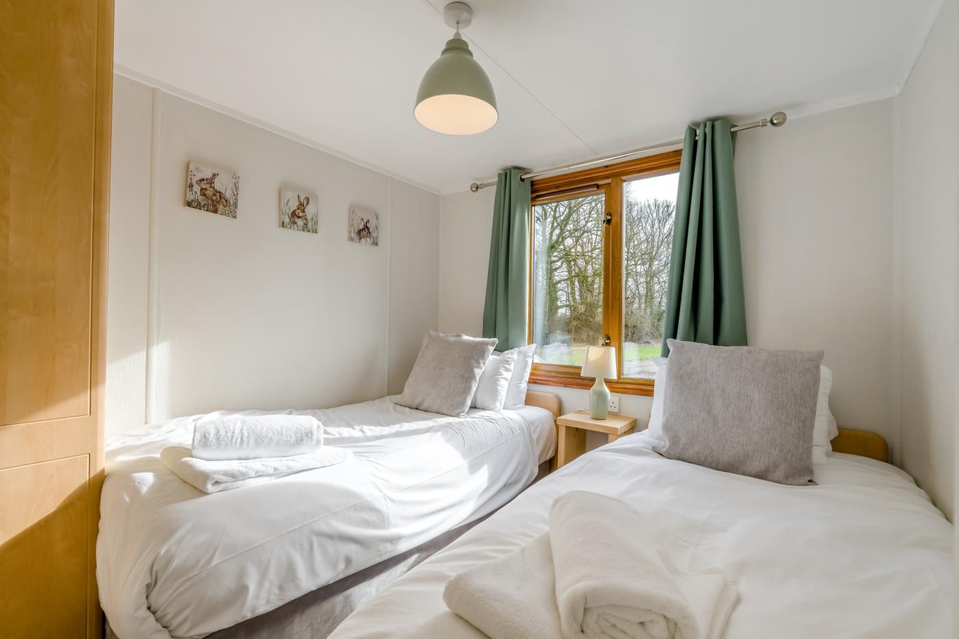 A room with two beds, a wooden wardrobe, a window with curtains, and wall art.