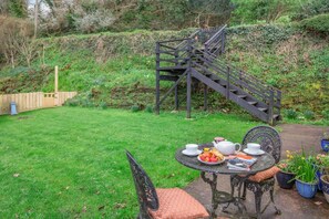 A garden with a table set for tea, a wooden fence, and a staircase leading up a hill. - 1 Bed in Bodinnick (oc-j38235) (Fowey)