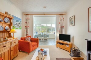 A living room with a sofa, TV stand, and a dining area with a table and chairs. - 1 Bed in Bodinnick (oc-j38235) (Fowey)
