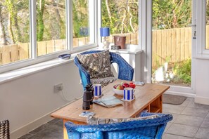 A sunlit room with a wooden table, wicker chairs, and a view of greenery outside. - 1 Bed in Bodinnick (oc-j38235) (Fowey)