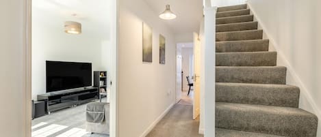 Ein Flur mit Treppe, Fernseher und Bücherregal.