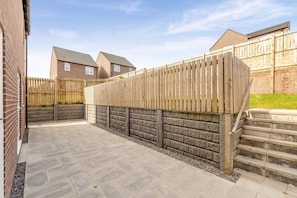 A patio with stone tiles, a wooden fence, and a brick wall. - 3 Bed in Aspatria (oc-h38206) (Aspatria)