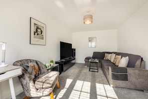A modern living room with a sofa, a television, a small table, and a chair. - 3 Bed in Aspatria (oc-h38206) (Aspatria)