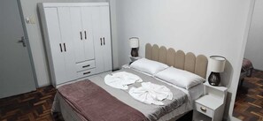 Un dormitori amb un llit, taules de nit, un armari i una porta.
