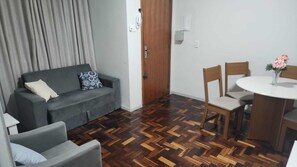 Habitació amb un sofà gris, una taula de dinar de fusta i cadires, i un paviment de fusta amb un disseny d'espiga.