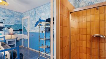 A room with a blue and white nautical-themed wall, a wooden door with a shower, and a bed with a blue headboard.