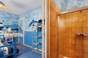 Une chambre avec un mur décoré dans le style marin, aux couleurs bleu et blanc, une porte en bois donnant sur une douche, et un lit avec une tête de lit bleue.