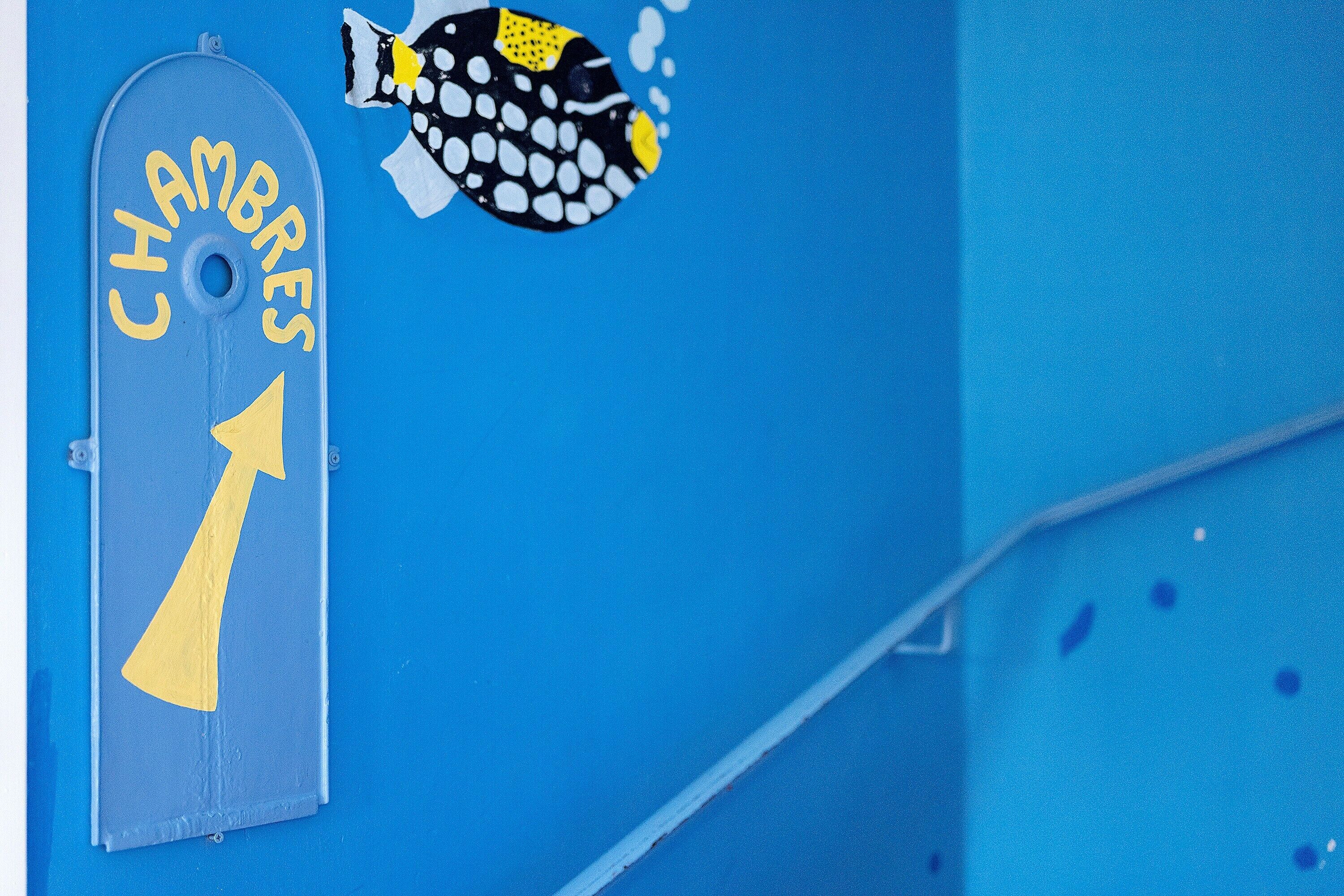 Eine blaue Wand mit einem Fisch-Aufkleber und dem Schriftzug 'CHANDRES' mit einem nach oben zeigenden Pfeil.