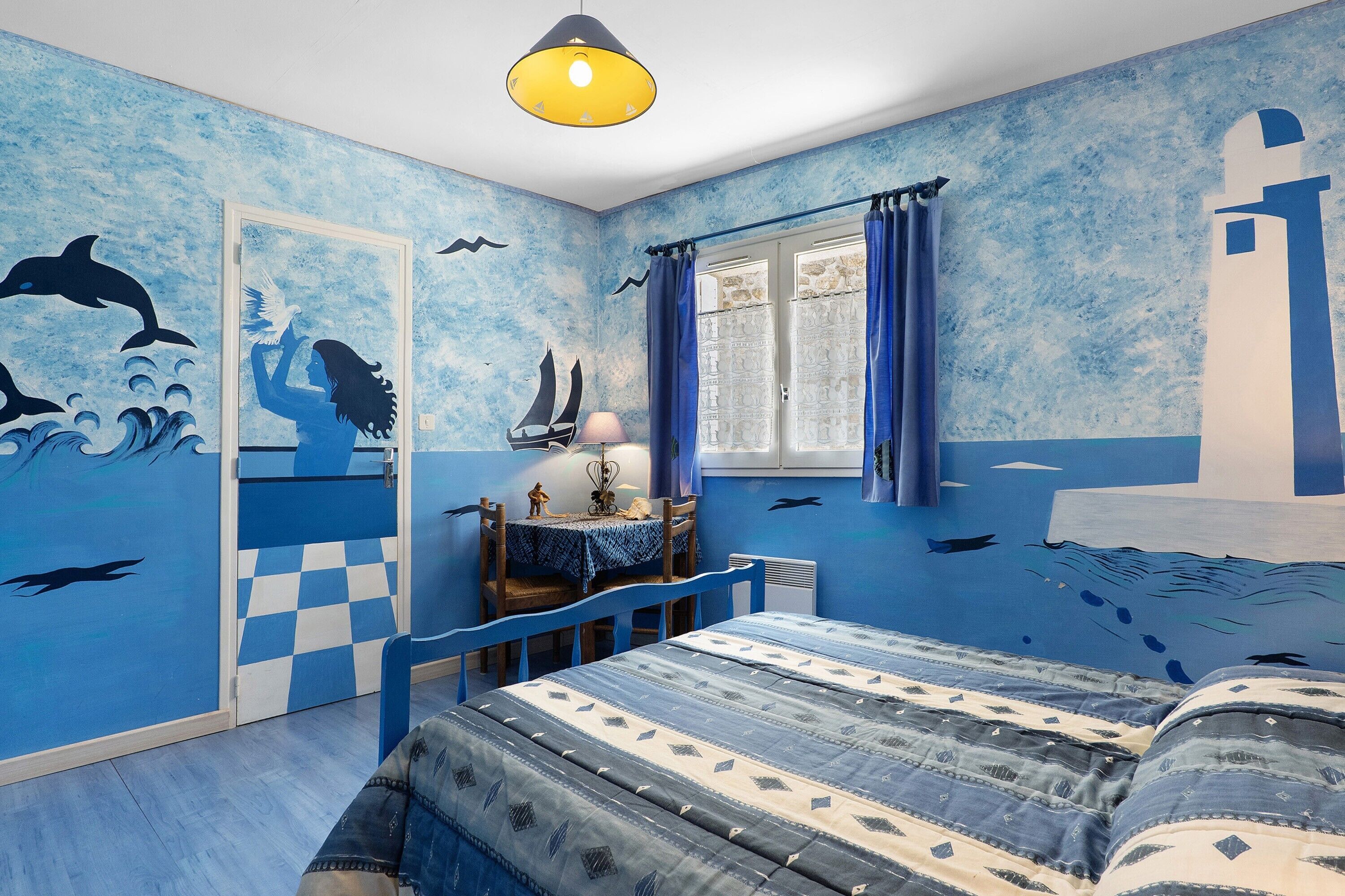 Een kamer met een bed, een tafel en een stoel. Er is een raam met gordijnen.