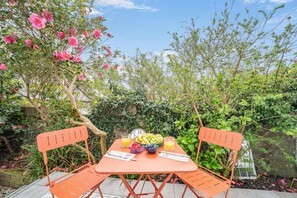 An outdoor dining area with a table set for two, surrounded by lush greenery and flowering plants. - 1 Bed in Wigtown (oc-b37520) (Wigtown)