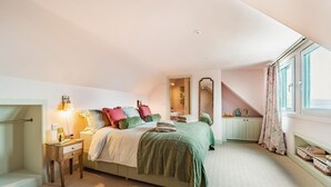 Une chambre à coucher avec un lit, des tables de chevet, un miroir, une fenêtre avec des rideaux et une vue sur l’extérieur.