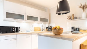 A modern kitchen with white cabinetry, a wooden island, a black pendant light, and a bowl of fruit. - Seebrücke Vacation Rental – Stay Close to the Beach with a Guarantee of Comfort (Wustrow)