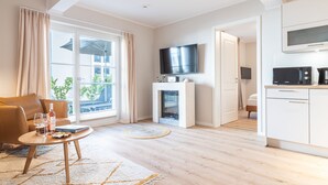 A modern living room with a sofa, a TV, a fireplace, and a kitchen area. - Seebrücke Vacation Rental – Stay Close to the Beach with a Guarantee of Comfort (Wustrow)