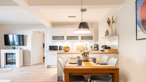 A modern kitchen with white cabinets, a dining table with chairs, and a TV in the adjacent room. - Seebrücke Vacation Rental – Stay Close to the Beach with a Guarantee of Comfort (Wustrow)