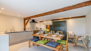 Une cuisine moderne avec des poutres en bois, une table à manger pour quatre personnes et un coin salon confortable avec un canapé et des fauteuils.