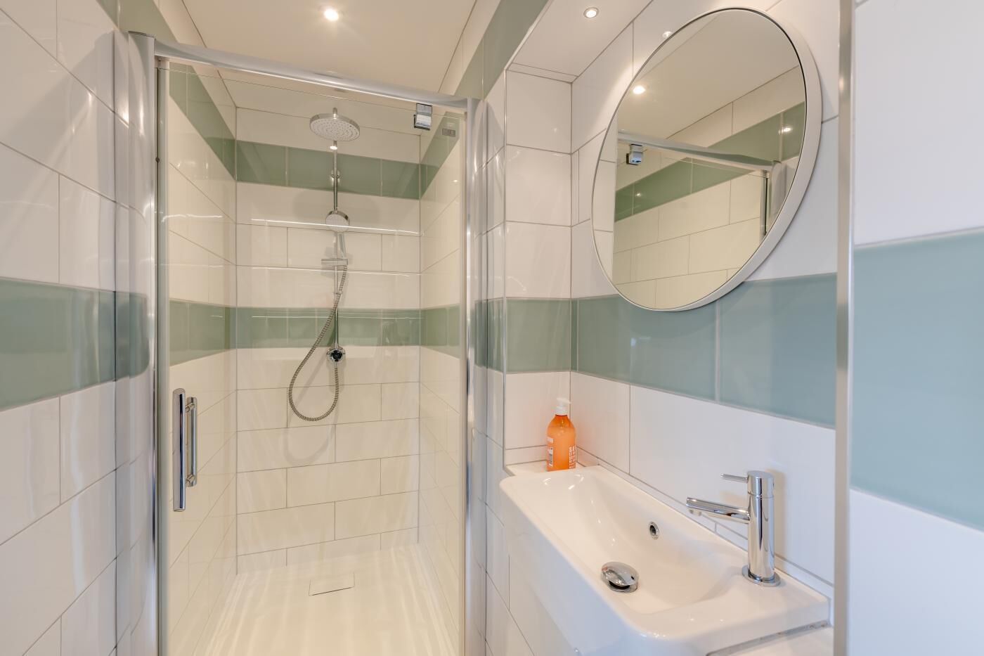 A modern bathroom with a glass-enclosed shower, a white sink with a mirror, and green-striped tiles.