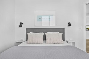A modern bedroom with a bed, two bedside tables, a wall-mounted light fixture, and a framed picture. - MeerWeite Holiday Apartment: Luxury & Stunning Sea Views Right by the Coast (Wendtorf)