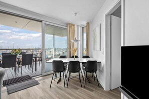 Ein moderner Essbereich mit Blick auf die Marina, ausgestattet mit einem Tisch, Stühlen, einem großen Fenster mit Vorhängen und einem Flachbildfernseher.