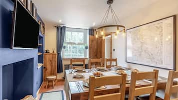 A dining area with a wooden table set for four, a large map on the wall, and a television mounted on the wall.