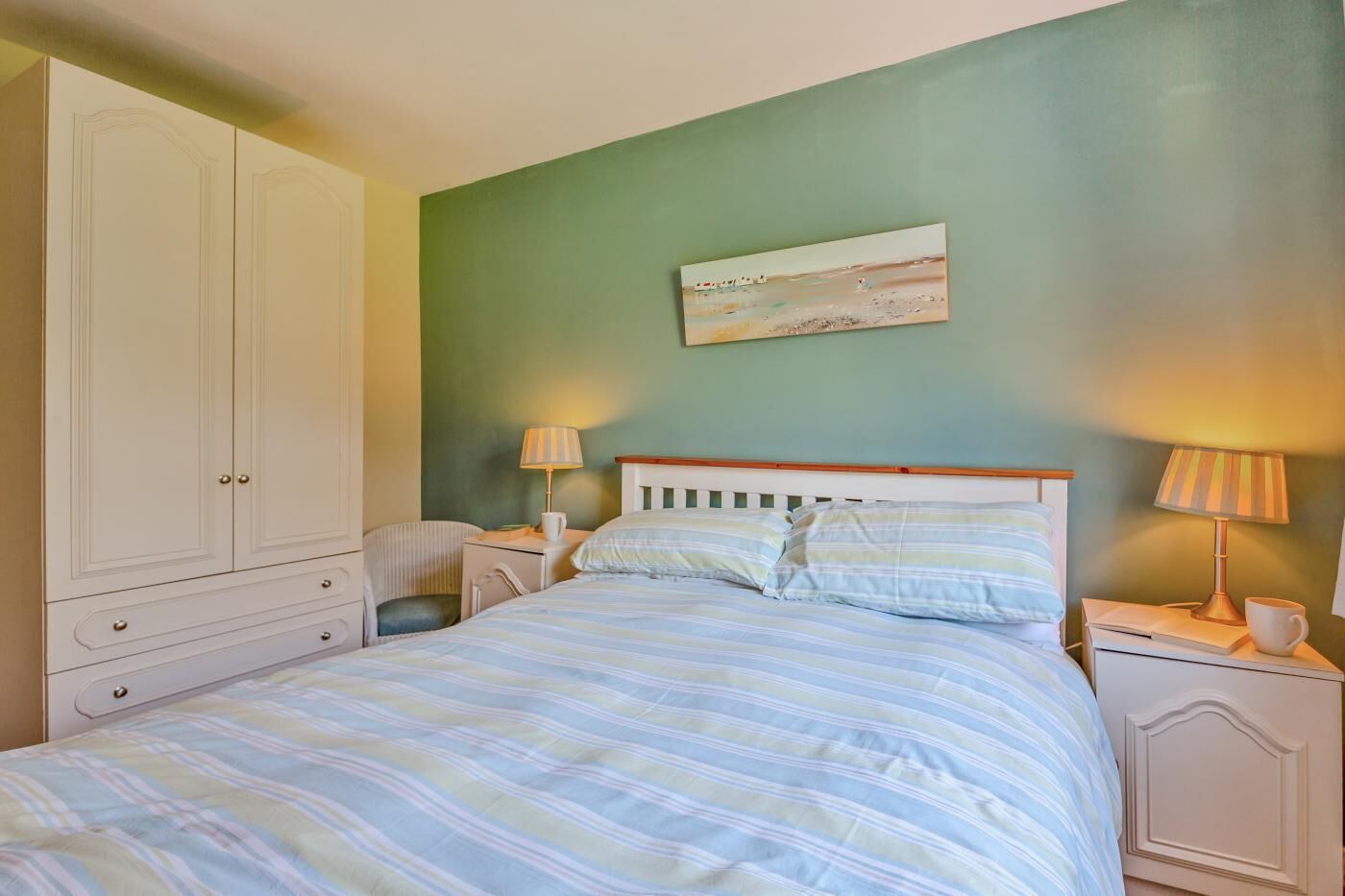 A bedroom with a bed, nightstands, a chair, a wardrobe, and a painting on the wall.
