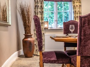 A dining area with a table set for two, a vase of dried plants, and a window with a view of greenery. - 6 Bed in Okehampton (oc-77877) (Lydford)