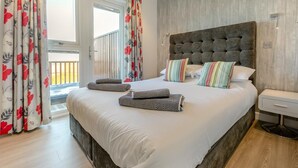 Une chambre avec un grand lit, une tête de lit en bois et un balcon agrémenté de rideaux.