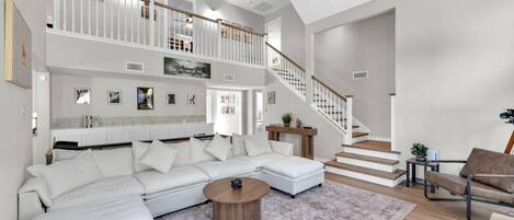 A spacious living room with a white sectional sofa, a wooden coffee table, and a staircase leading to an upper level.