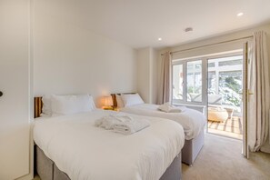A hotel room with two beds, a window with curtains, a balcony with a sofa, and a view of the outdoors. - 4 Bed in Aberdovey (oc-c35170) (Aberdovey)