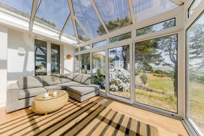 Ein modernes Wohnzimmer mit einem Ecksofa, einem runden Couchtisch und großen, vom Boden bis zur Decke reichenden Fenstern mit Blick ins Freie.