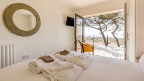 Quarto com cama, um espelho grande, televisão e vista para a praia através de uma porta aberta.
