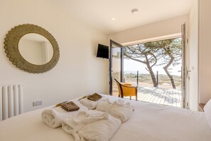 Ein Schlafzimmer mit Bett, einem großen Spiegel, einem Fernseher und Blick auf den Strand durch eine offene Tür.