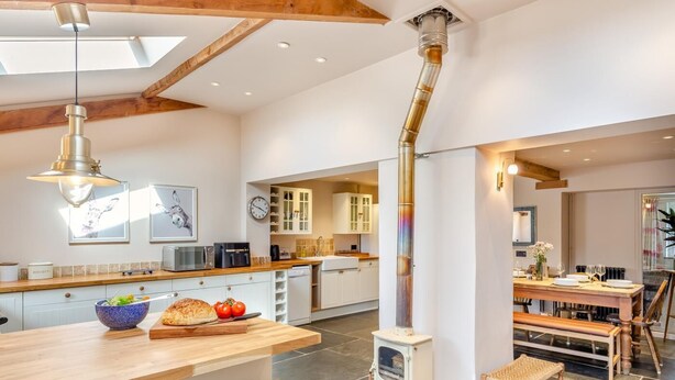 A modern kitchen with a central island, a dining area with wooden furniture, and a visible chimney. - 3 Bed in Holcombe Rogus (oc-a39001) (Holcombe Rogus)