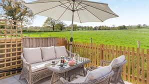 A patio with wicker furniture, a table with drinks, and a large umbrella. - 3 Bed in Holcombe Rogus (oc-a39001) (Holcombe Rogus)