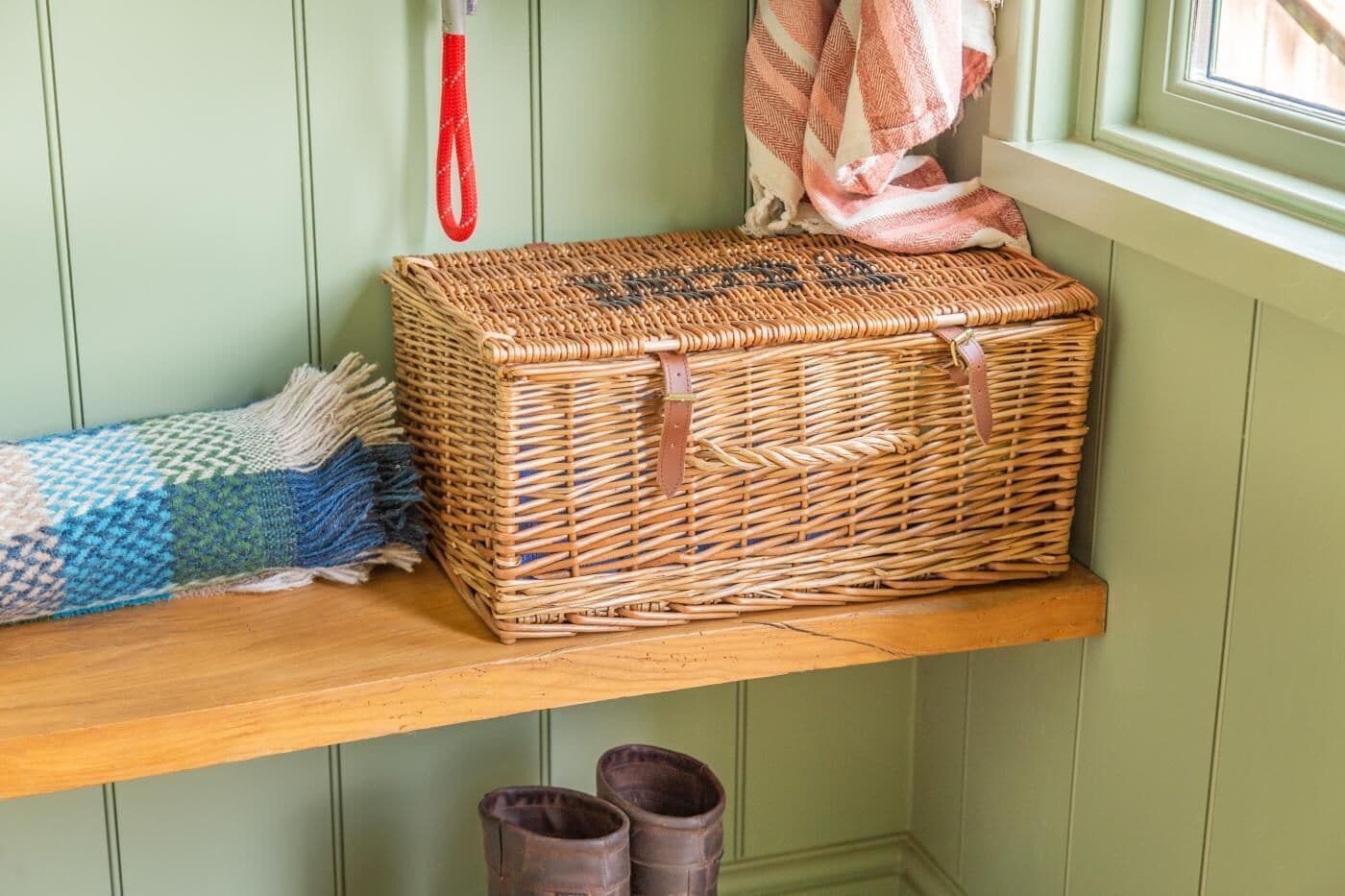 A wicker basket on a shelf, a woven blanket, and a pair of boots.